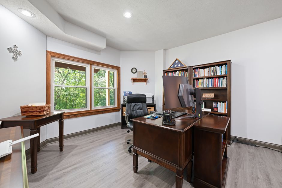 A bright, stylish home office featuring a wooden desk and bookshelves with a view of nature outside.